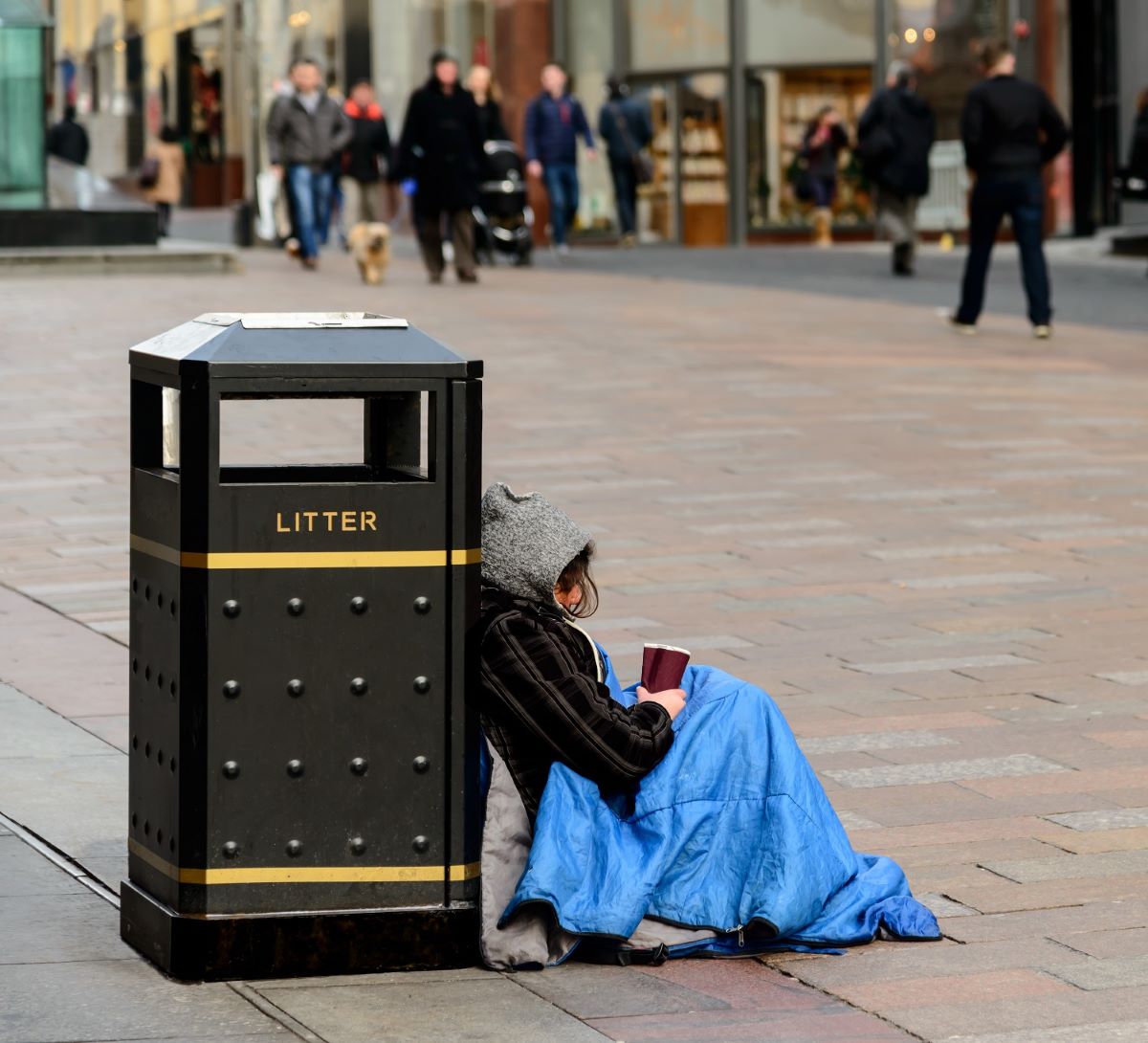 homeless person in sleeping bag sat against bin