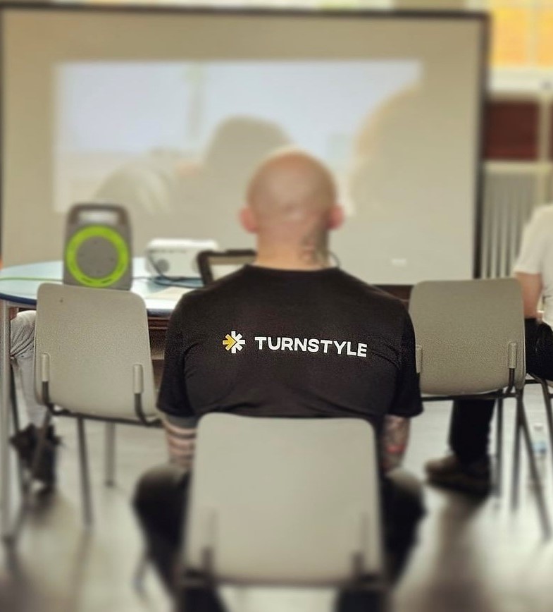 Man sat in a chair, Turnstyle logo on t-shirt